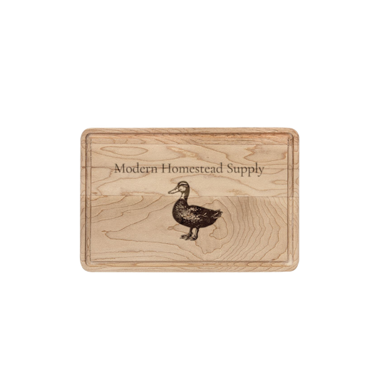 Wooden cutting board with 'Modern Homestead Supply' branding and duck illustration on a white background