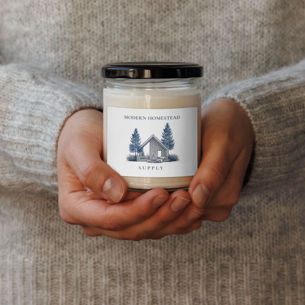 Person holding a candle jar labeled 'Modern Homestead Supply' against a neutral background
