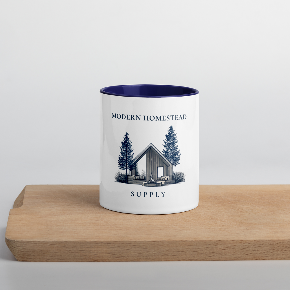 White mug with blue interior and 'Modern Homestead Supply' design on a wooden surface.